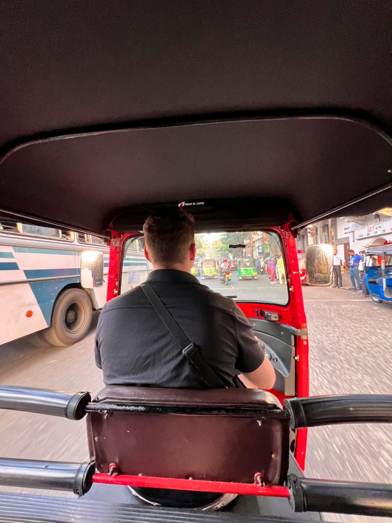 Interior view of a tuk tuk in Sri Lanka from the passenger seat, with the driver navigating city roads.
