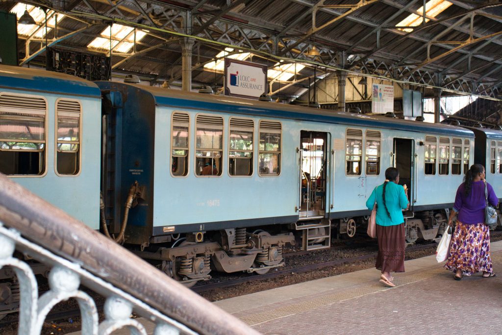 Colombo Fort railway station in Sri Lanka, with two local women eating ice cream in front of a blue train on the track.