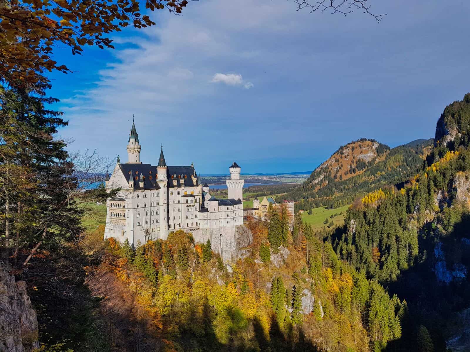 Neuschwanstein Castle surrounded by colorful autumn foliage on a sunny day, seen from outside — a must-do day trip from Munich.
