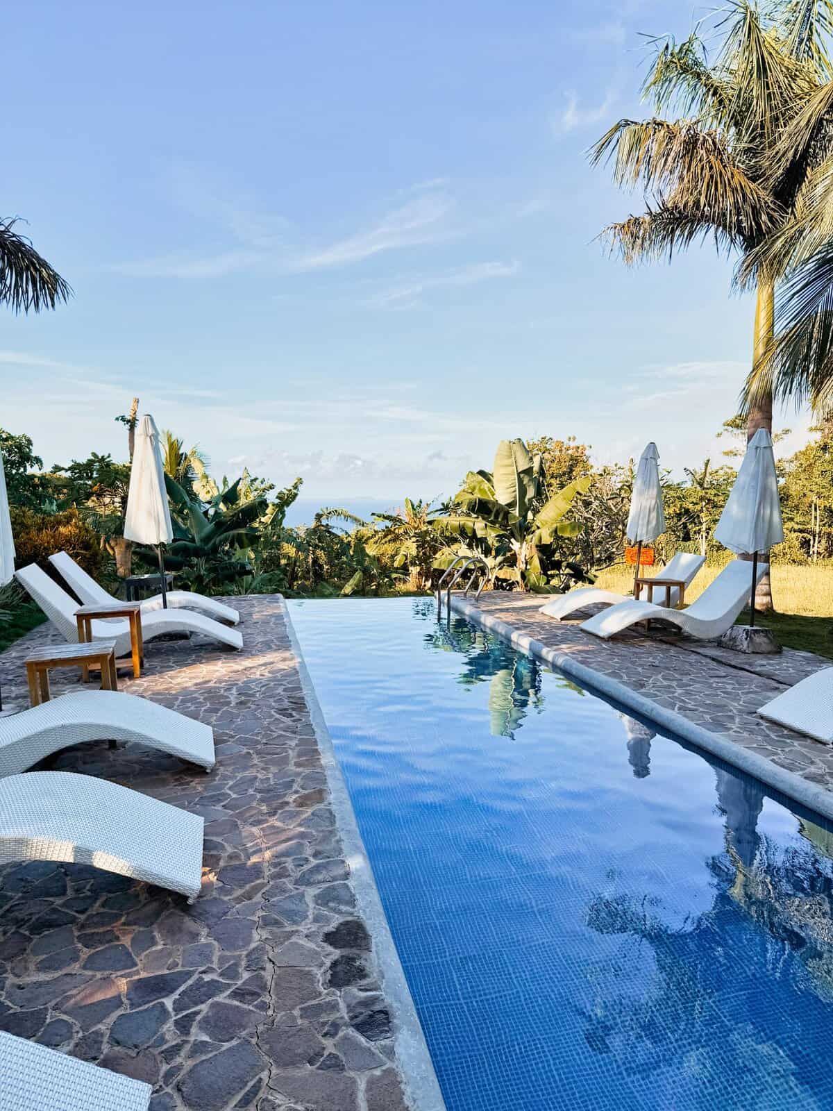 Infinity pool at South Mountain Resort in San Juan Siquijor with white loungers and umbrellas overlooking lush tropical greenery and the ocean in the distance. The serene pool setting shows why this hillside resort is a relaxing place to stay in Siquijor while exploring the island.