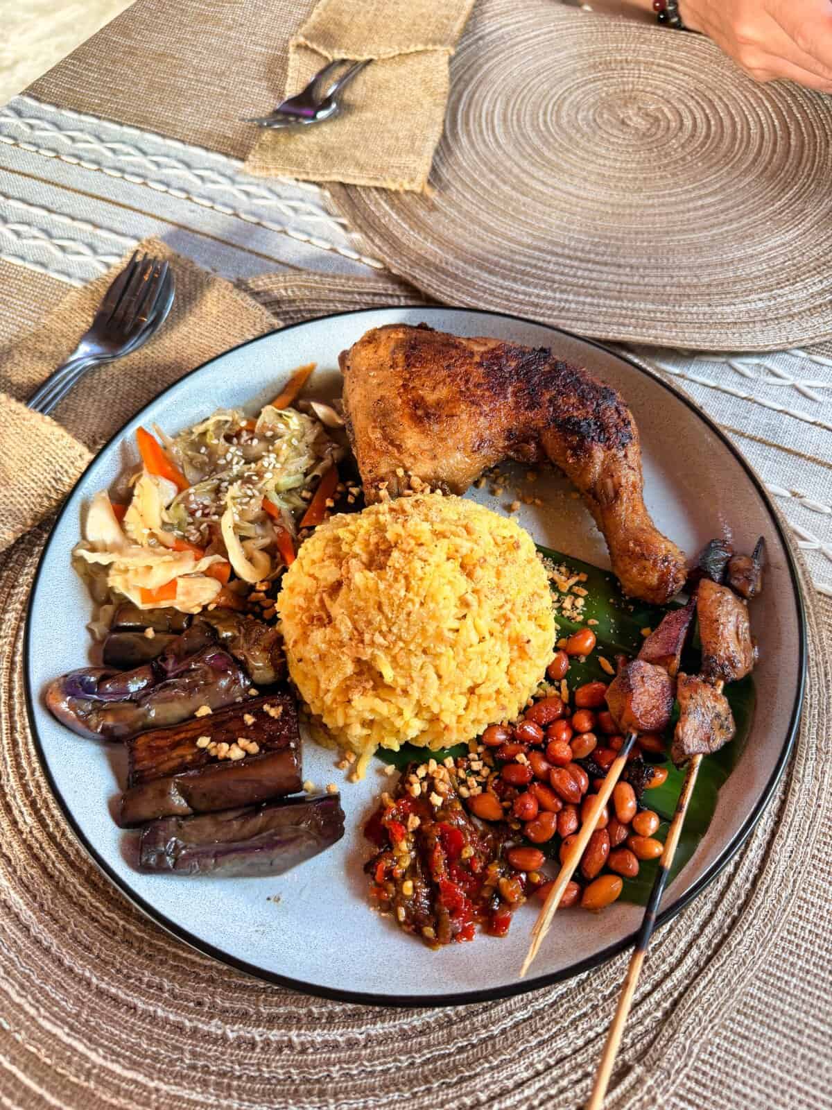 A generous plate of Indonesian food at Warung Balay in San Juan, Siquijor features yellow rice, grilled chicken, skewers, vegetables, peanuts, and sambal. The overhead view highlights the large portions and variety that make this spot popular with travelers in Siquijor.