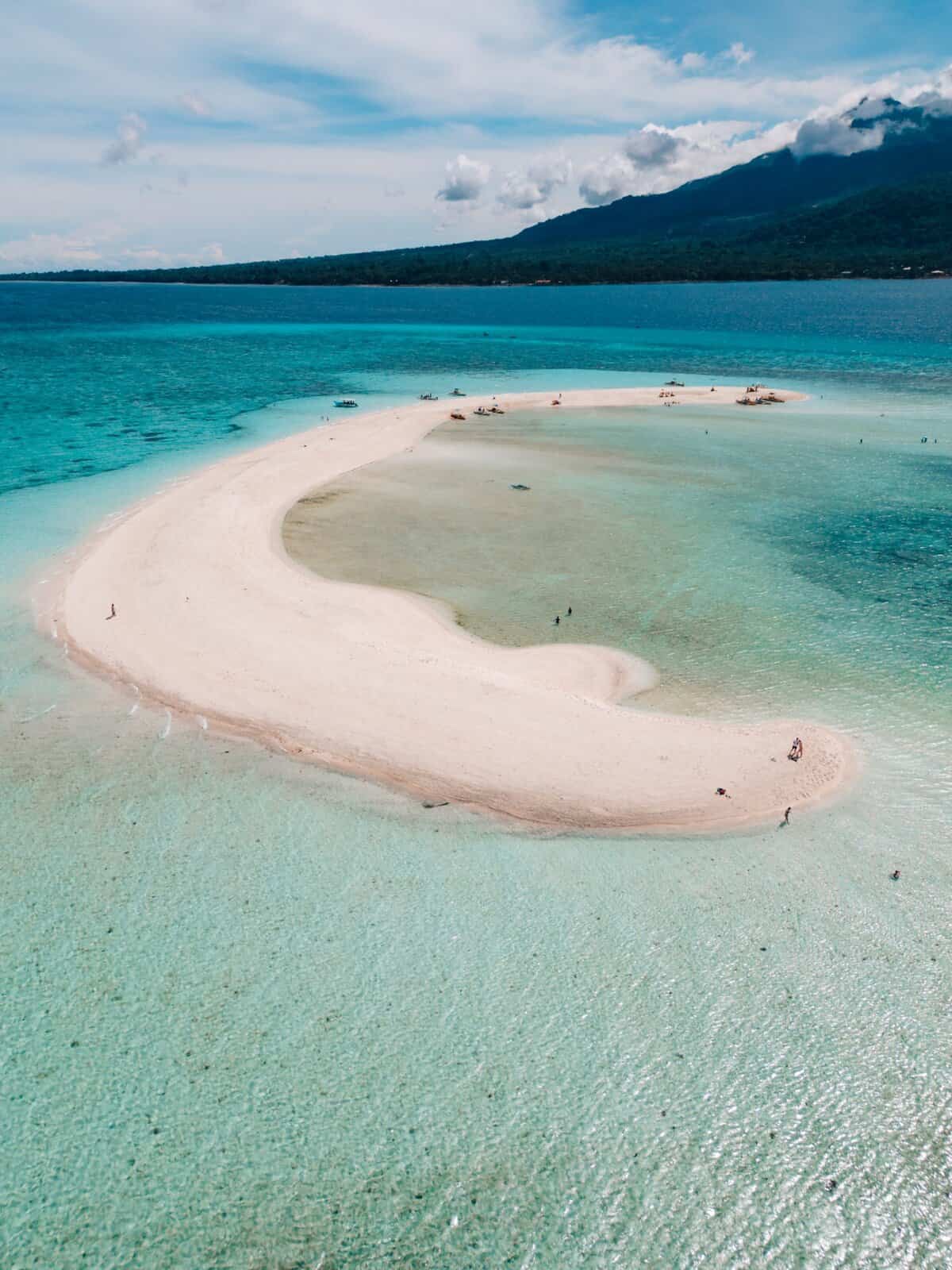 White sandbank as seen from a drone with Camiguin island in the distance, surrounded by turquise waters.