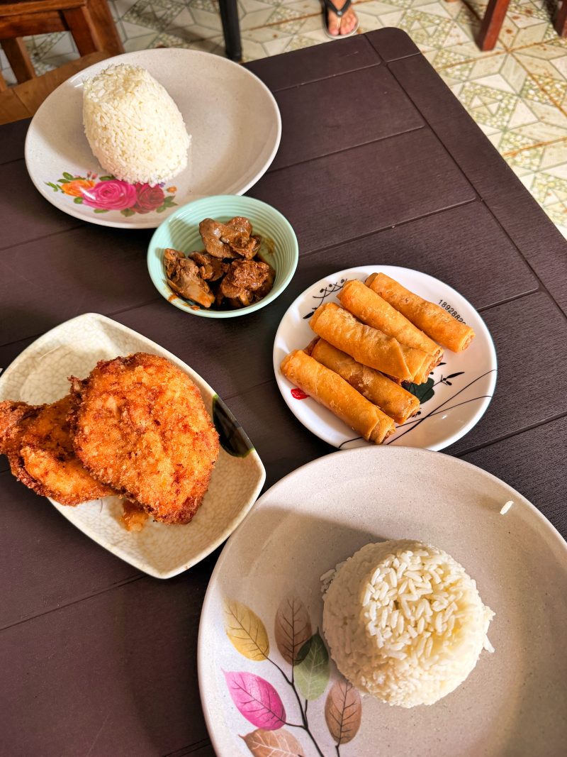 Plates of local Filipino dishes served on a simple table at a casual eatery in Siquijor. Small local restaurants like this are common around San Juan where many travelers stay.