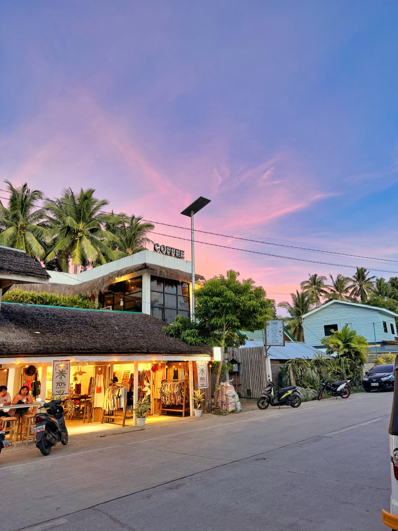 Evening street view in San Juan with pink sky and lights from a shop. This area is the main tourist hub and one of the most popular places to stay in Siquijor.
