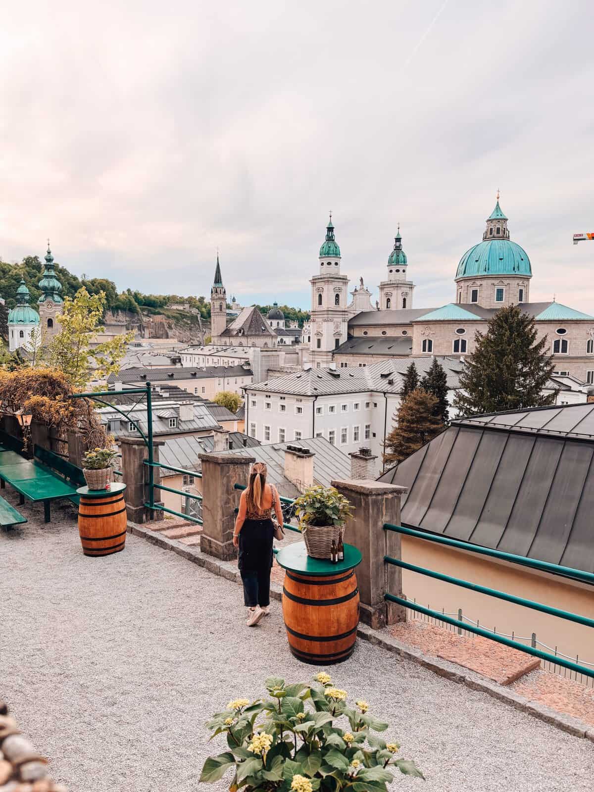 View over Salzburg's Old Town from a rooftop terrace, with the domes of Salzburg Cathedral and historic church towers in the background.
