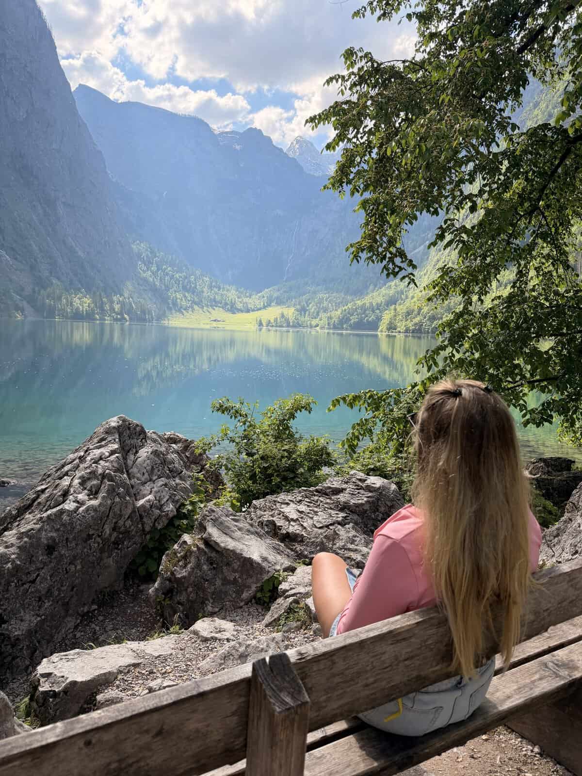 Woman sitting on a bench overlooking Obersee during a Lake Königssee hiking trip in Bavaria