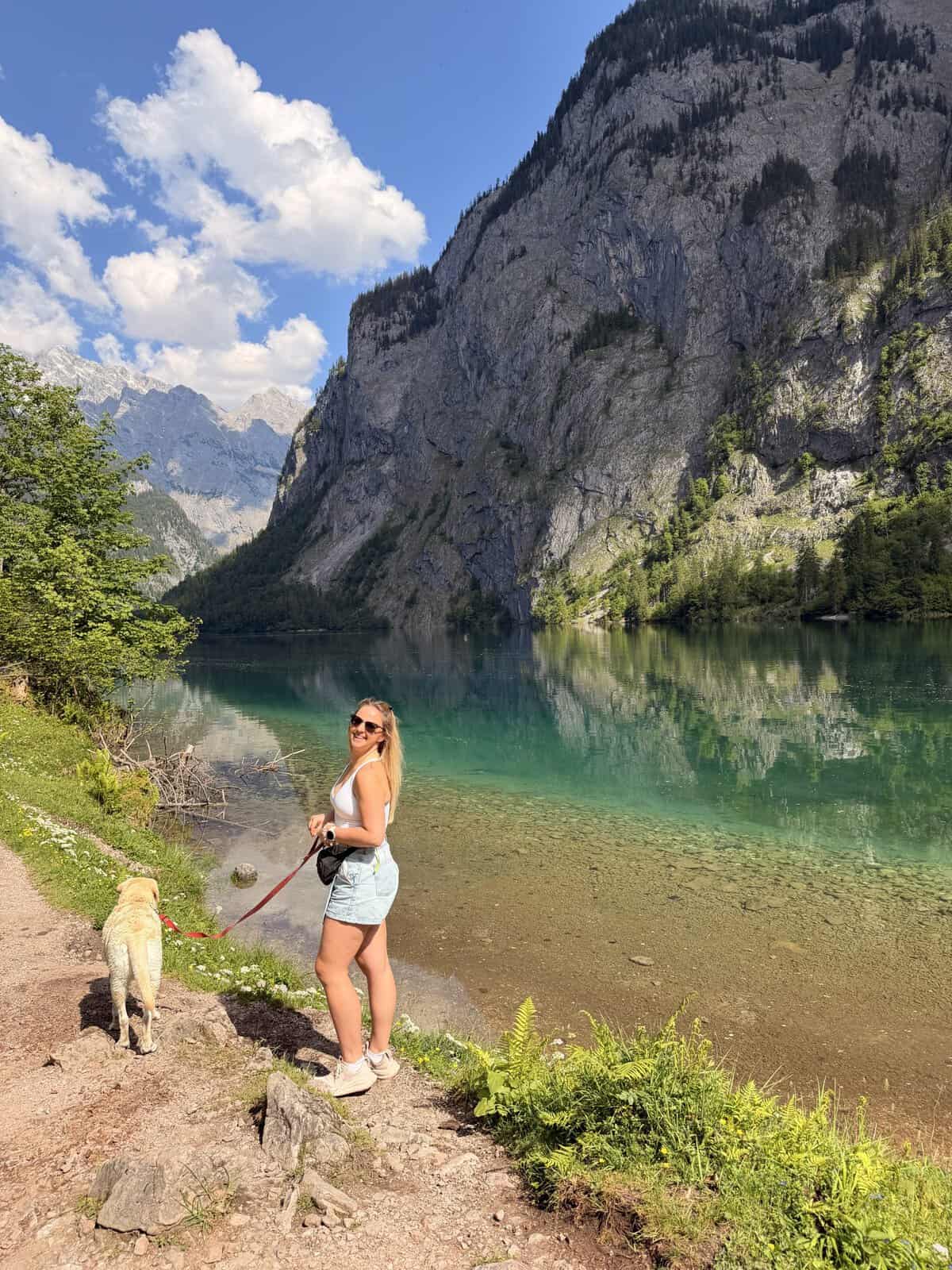 Woman hiking with her dog beside turquoise Obersee near Lake Königssee in Berchtesgaden National Park