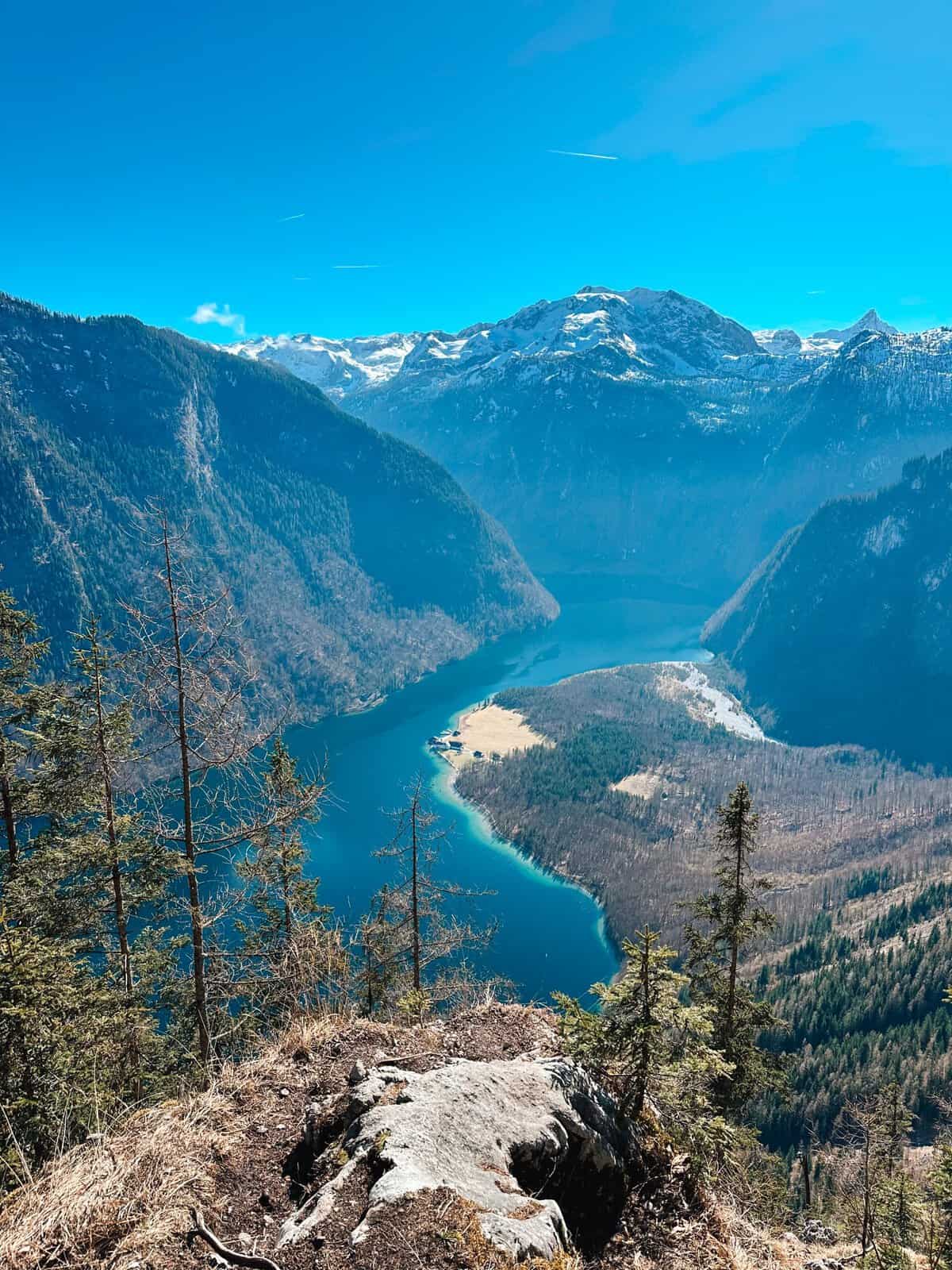 View of Königssee lake in the Berchtesgaden Alps, with turquoise water winding through forested mountains beneath snow-capped peaks.