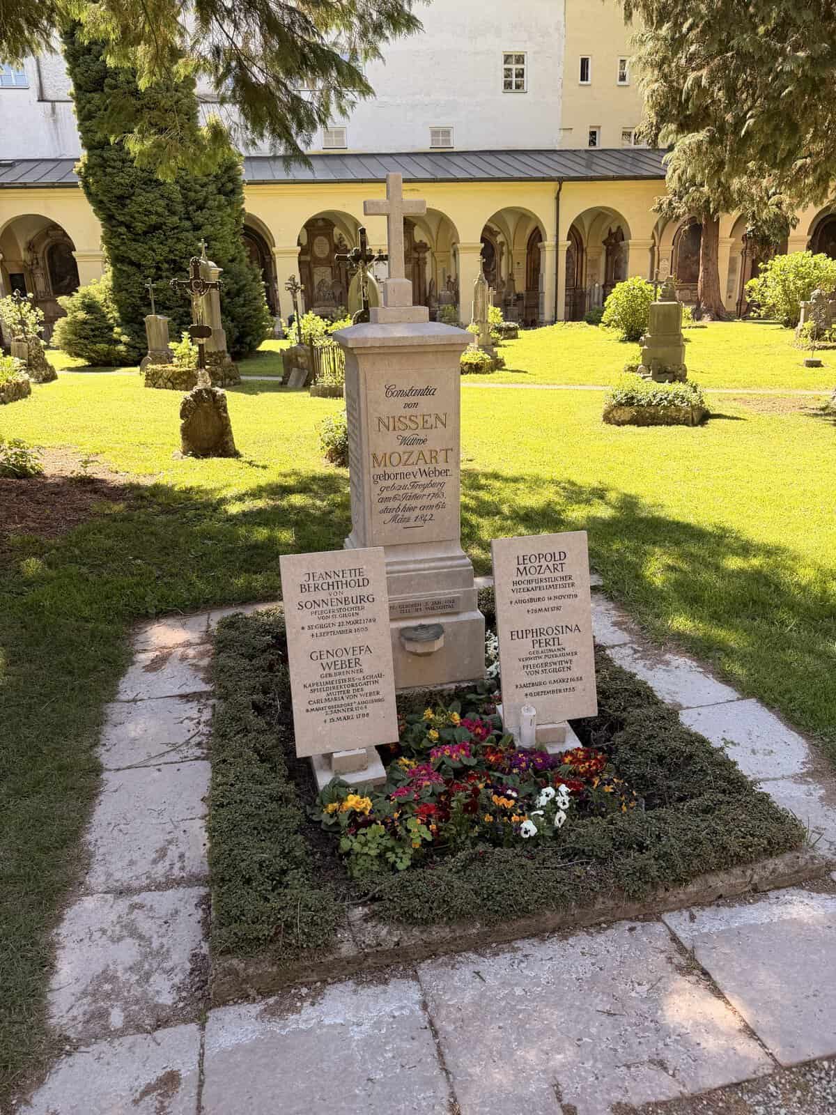 Mozart family graves at St. Sebastian Cemetery in Salzburg, including memorials for Constanze Mozart, Leopold Mozart, and other relatives in a peaceful cloister garden.
